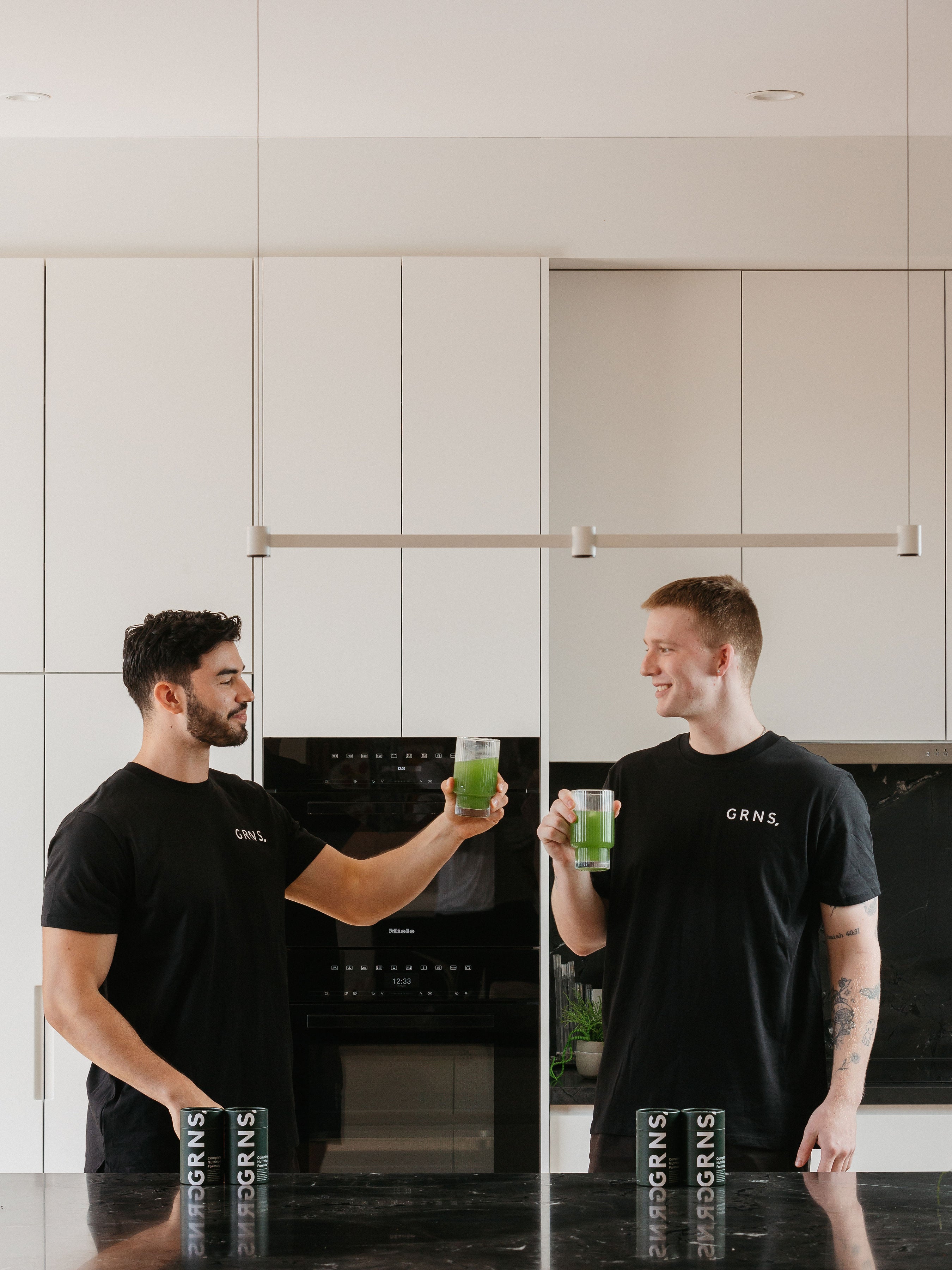 Two friends smiling and looking healthy holding greens powder liquid in their glasses