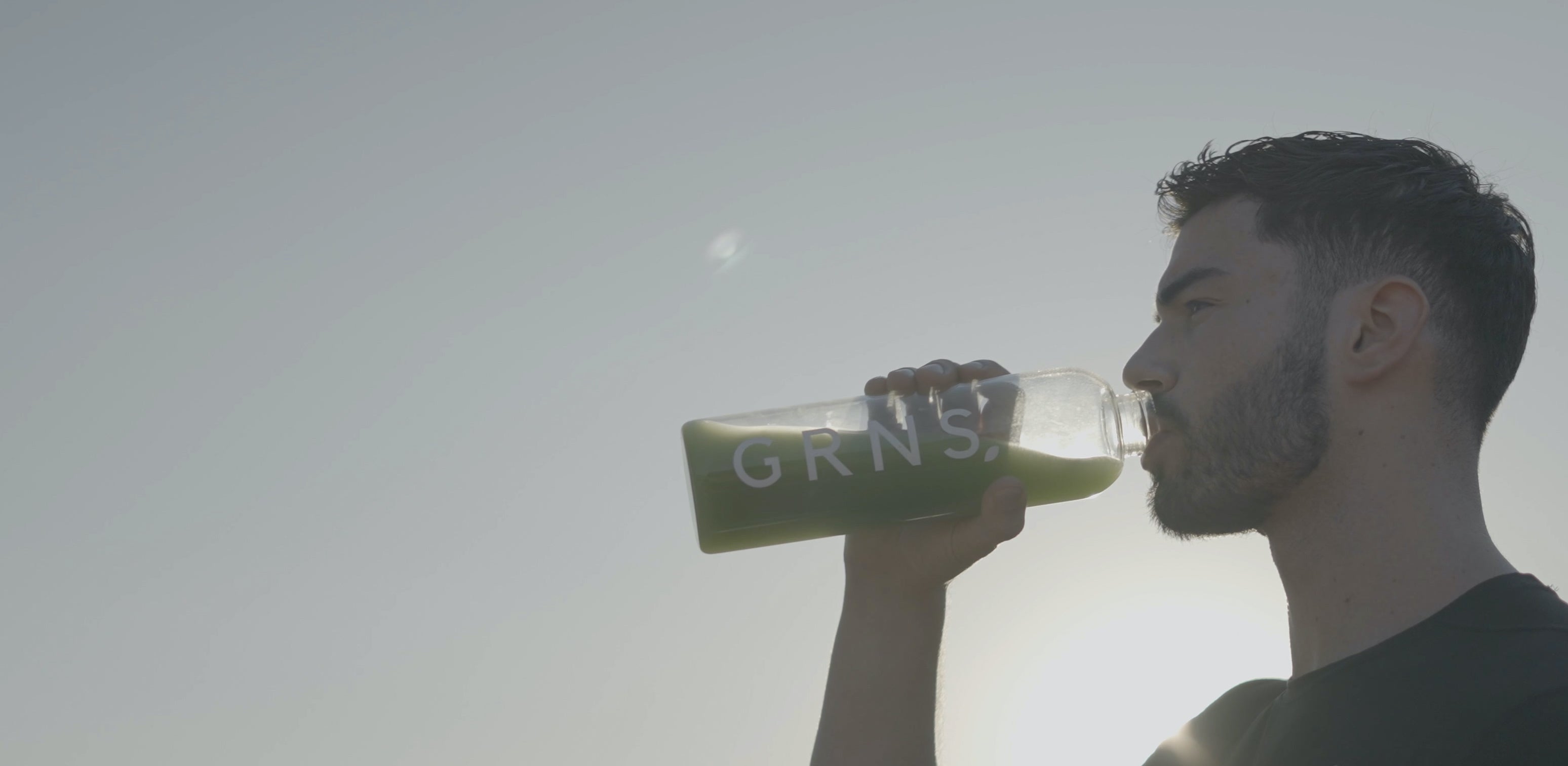 An athletic man drinking a bottle with a greens powder supplement drink inside that helps with gut health energy skin and has over 40 superfoods greens, anda woman drinking her greens powder drink in a living room with a healthy atmosphere